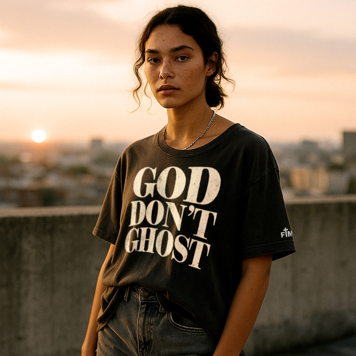 Person wearing a t-shirt with 'GOD DON'T GHOST' text against a sunset cityscape.