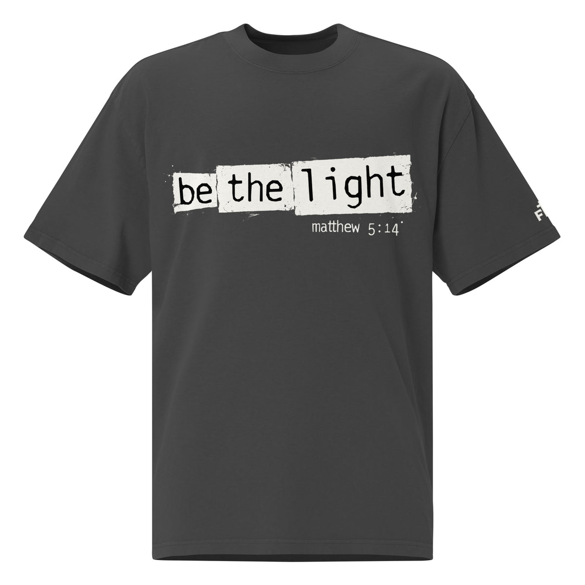 Front view of a Faded Black oversized tee featuring Be the Light in black typewriter lettering over distressed cream panels, Matthew 5:14, and a small sleeve logo.