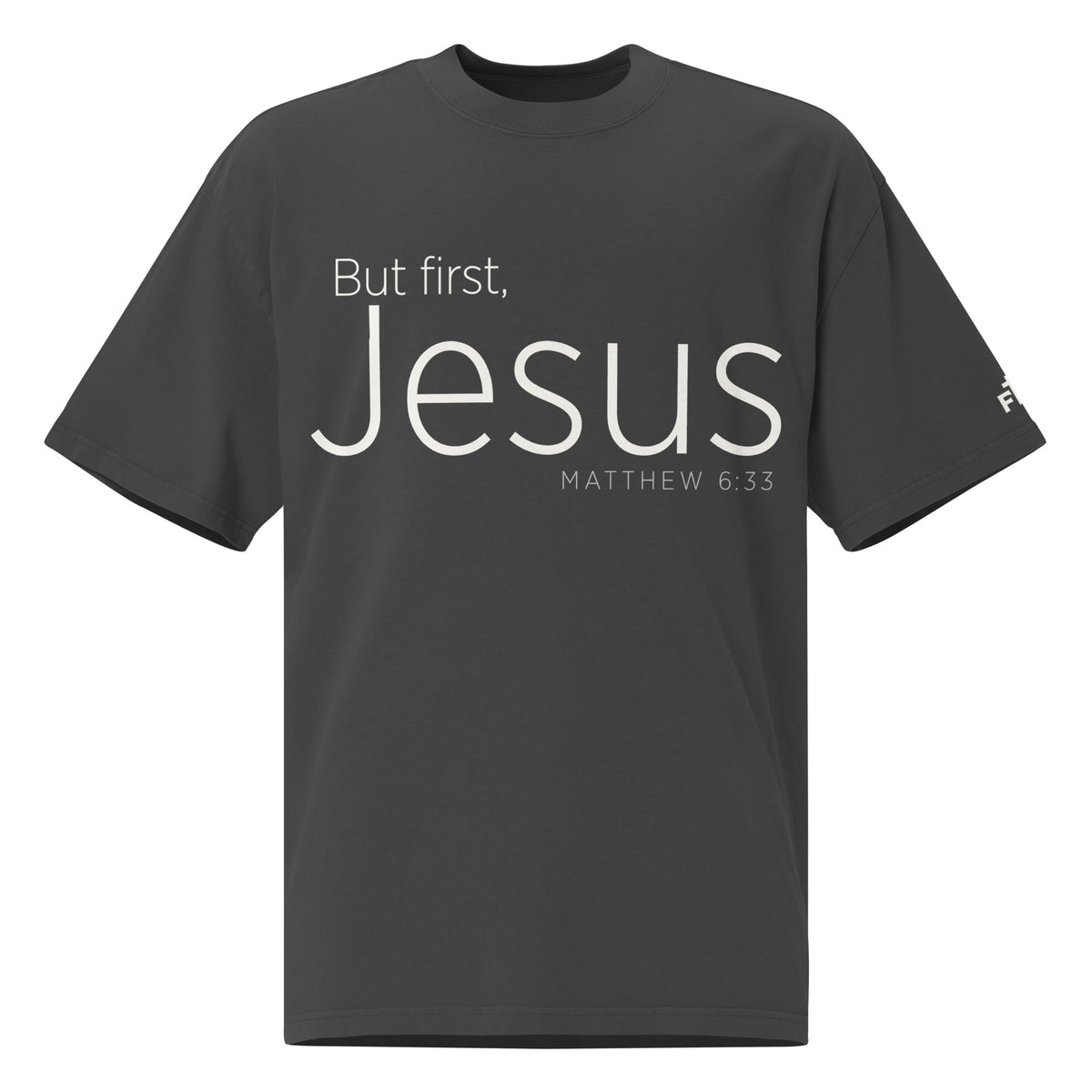 Front view of a Faded Black oversized tee featuring cream But First, Jesus lettering, Matthew 6:33, and a small Faith Mode logo on the left sleeve.