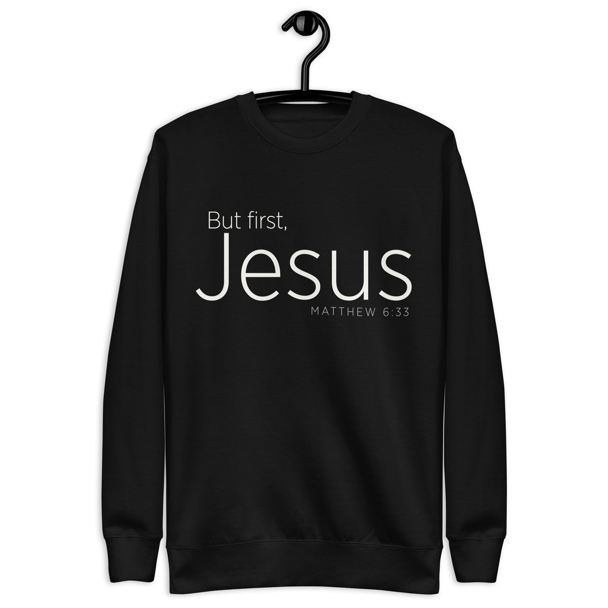 Black unisex sweatshirt with cream-white “But First, Jesus” typography and Matthew 6:33 printed on the front. Hanger view.