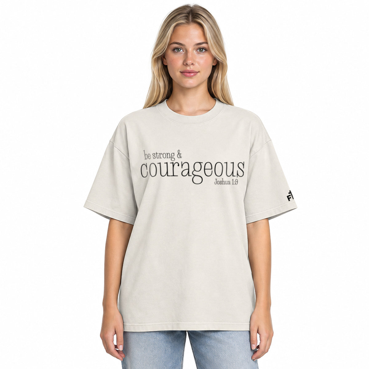 Front view of a faded bone oversized tee featuring black Be Strong & Courageous lettering, Joshua 1:9, and a small Faith Mode logo on the left sleeve.
