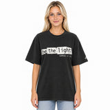 Front view of a Faded Black oversized tee featuring Be the Light in black typewriter lettering over distressed cream panels, Matthew 5:14, and a small sleeve logo.
