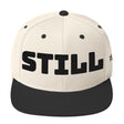Beige cap with black 'STILL' text on a white background