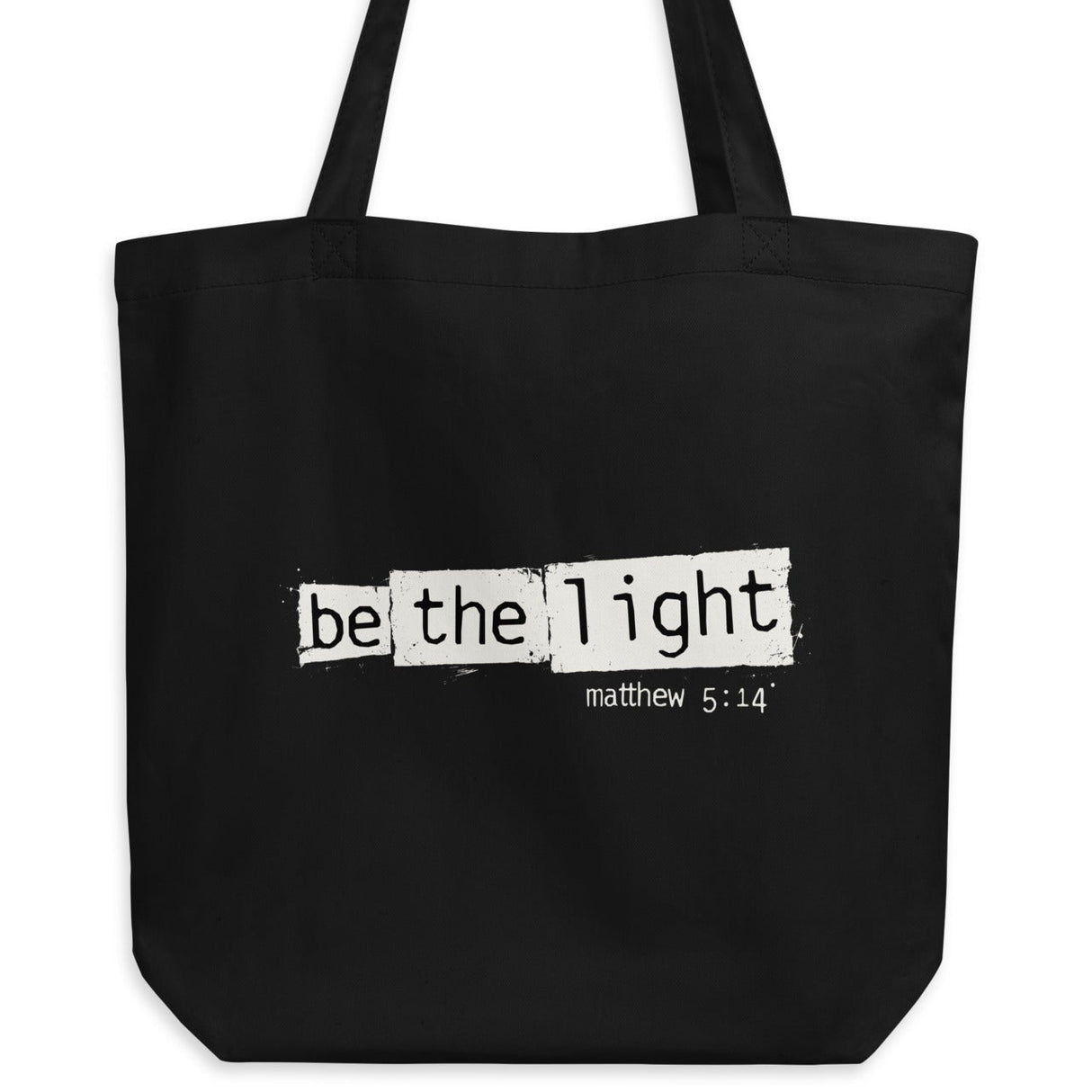 Black eco tote bag featuring a distressed cream-white “Be the Light” design with Matthew 5:14.