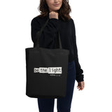 Black eco tote bag featuring a distressed cream-white “Be the Light” design with Matthew 5:14.