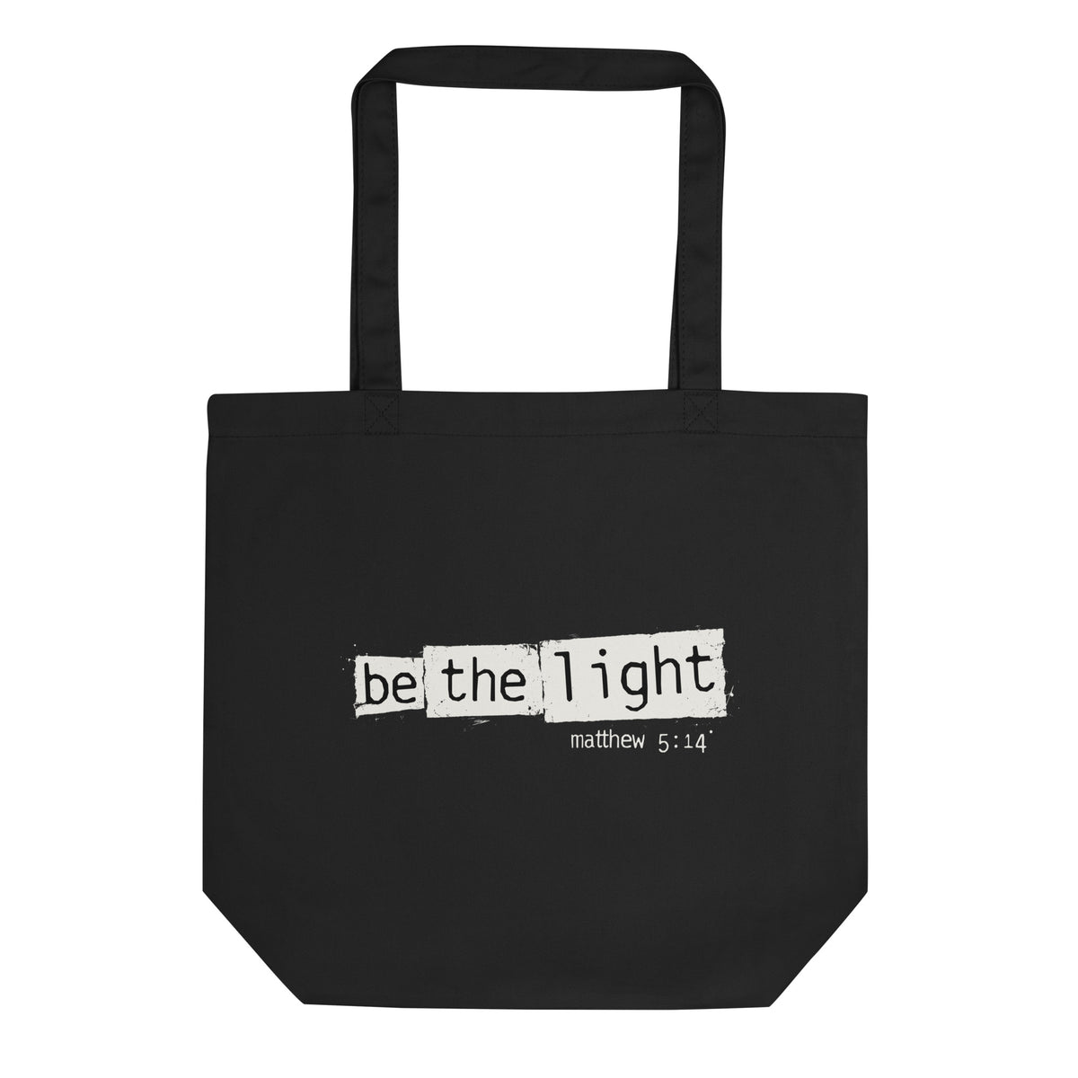 Black eco tote bag featuring a distressed cream-white “Be the Light” design with Matthew 5:14.