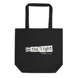 Black eco tote bag featuring a distressed cream-white “Be the Light” design with Matthew 5:14.