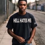 Person wearing a garment-dyed black t-shirt with 'HELL HATES ME' text on a street.