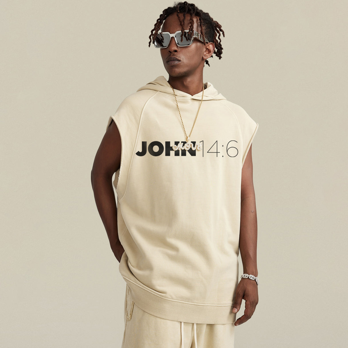 Person wearing a beige sleeveless hoodie with 'JOHN 14:6' text on a plain background