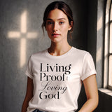 Woman wearing a white t-shirt with 'Living Proof of Loving God' text in a room with a cross on the wall.