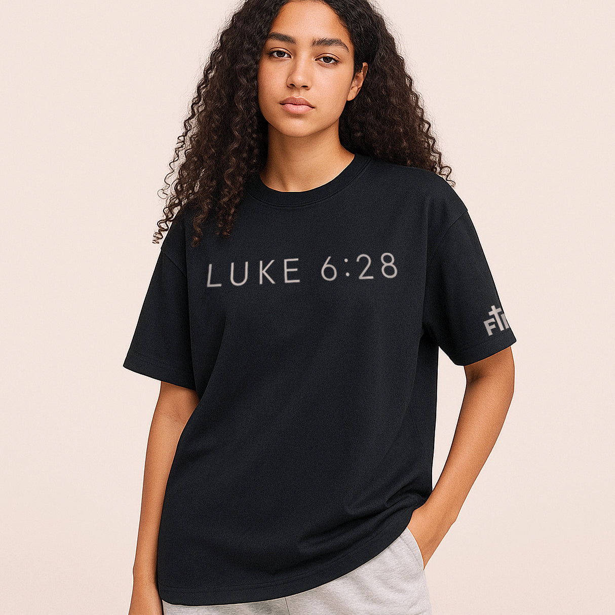 Person wearing a black t-shirt with 'LUKE 6:28' text on a beige background