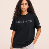 Person wearing a black t-shirt with 'LUKE 6:28' text on a beige background