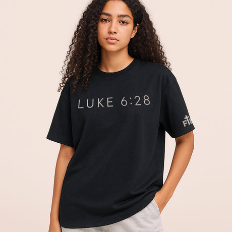 Person wearing a black t-shirt with 'LUKE 6:28' text on a beige background