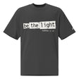 Front view of a Faded Black oversized tee featuring Be the Light in black typewriter lettering over distressed cream panels, Matthew 5:14, and a small sleeve logo.