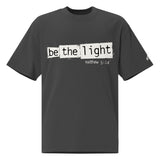 Front view of a Faded Black oversized tee featuring Be the Light in black typewriter lettering over distressed cream panels, Matthew 5:14, and a small sleeve logo.