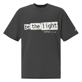 Front view of a Faded Black oversized tee featuring Be the Light in black typewriter lettering over distressed cream panels, Matthew 5:14, and a small sleeve logo.