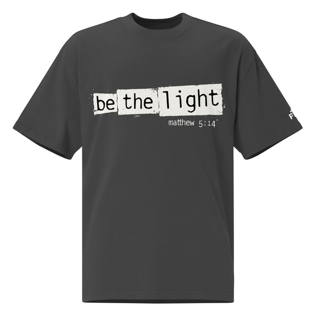 Front view of a Faded Black oversized tee featuring Be the Light in black typewriter lettering over distressed cream panels, Matthew 5:14, and a small sleeve logo.