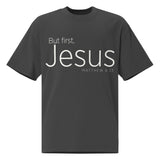Front view of a Faded Black oversized tee featuring cream But First, Jesus lettering, Matthew 6:33
