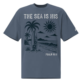 Front view of a Faded Indigo oversized tee featuring The Sea Is His, Psalm 95:5, palm trees, a surfboard, sun, ocean waves, and a small sleeve logo.