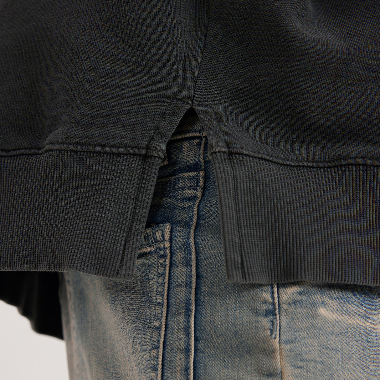Close-up of a black hoodie, showing the side-slit, and blue jeans on a white background