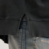 Close-up of a black hoodie, showing the side-slit, and blue jeans on a white background