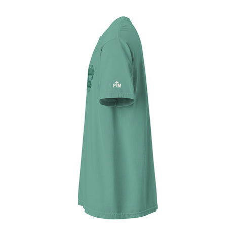 A sage green short-sleeve t-shirt shown from a side profile view against a solid white background. The shirt features a small white 'FM' logo on the right sleeve and a darker green graphic on the left chest.