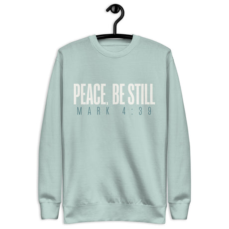 Agave blue unisex sweatshirt with cream-white “Peace, Be Still” lettering and Mark 4:39 printed beneath. Shown on hanger