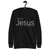 Black unisex sweatshirt with cream-white “But First, Jesus” typography and Matthew 6:33 printed on the front. Shown with hanger.