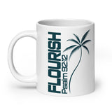 White glossy coffee mug with a left-side handle, featuring dark teal vertical FLOURISH lettering, Psalm 92:12, and a palm tree illustration.