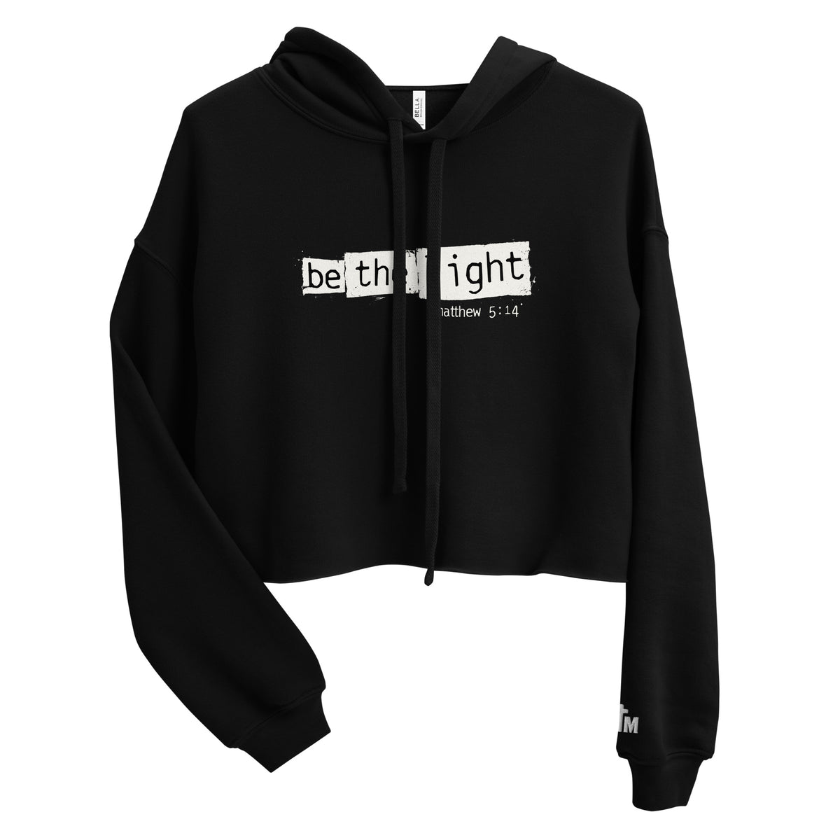 Front view of a black women’s crop hoodie with distressed white “Be The Light” lettering and Matthew 5:14 on the chest, a drawstring hood, and long sleeves.