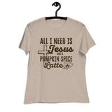 A beige short-sleeve t-shirt hanging on a black hanger against a white background, featuring a dark brown graphic print that reads 'ALL I NEED IS Jesus AND A PUMPKIN SPICE Latte' with a cross, coffee cup, and spice motif.