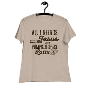 A beige short-sleeve t-shirt hanging on a black hanger against a white background, featuring a dark brown graphic print that reads 'ALL I NEED IS Jesus AND A PUMPKIN SPICE Latte' with a cross, coffee cup, and spice motif.